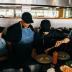 Tim chef profesional bekerja sama menyiapkan dan menyajikan hidangan di dapur restoran, menggambarkan operasional industri F&B